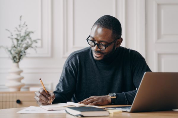 Male educator at desk reviewing notes near laptop
