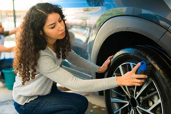 Young Hispanic woman checking air pressure in tire