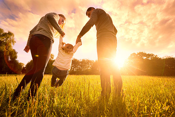 Family swinging toddler in sunshine outside
